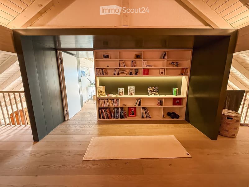 Bright, open room with wooden flooring, built-in bookshelf filled with books and decorative items, and a wicker basket near the wall.