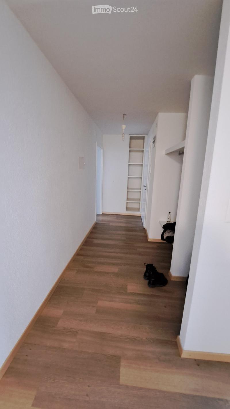 Empty hallway with wooden flooring, white walls, and a built-in shelf unit on the right side.
