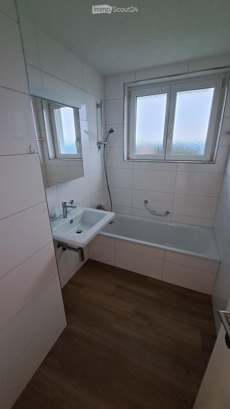 Modern bathroom with white tiles, a sink, bathtub, mirror, and showerhead. Features two windows with frosted glass panes.