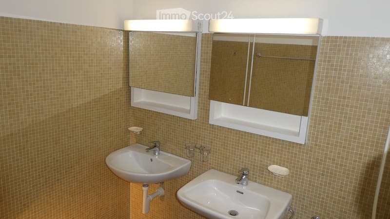 Two sinks, two mirrors, tiled walls, two faucets, glass containers, soap dish