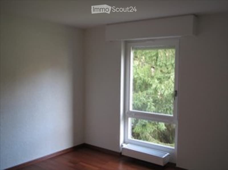 Completely empty room with bare walls, wooden floor, and a single window with white frame and white sill.