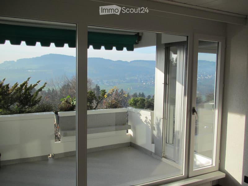 Balcony with large glass doors, white railings, and a scenic mountain view.