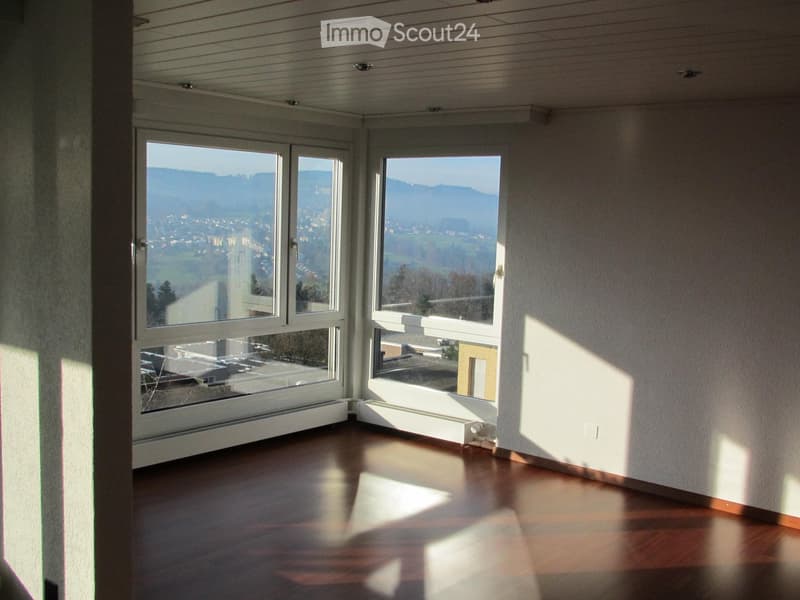 Empty room with wooden flooring, large windows offering a scenic view, and white walls.