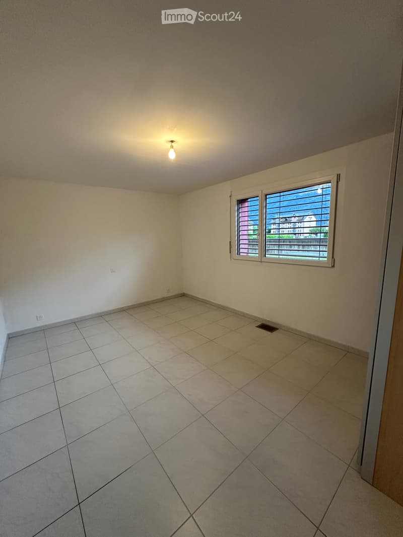 Empty room with tiled floor, white walls, and a single window with blinds. Natural light enters through the window, and the room has a ceiling light fixture.