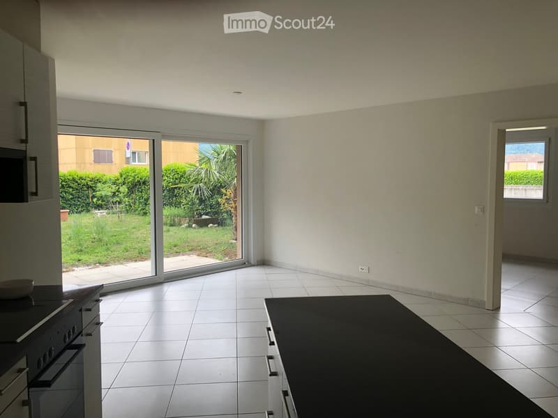 Modern kitchen with white tiled floor, black countertop, built-in oven, and sliding glass door leading to a garden.