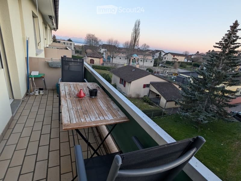 Balcony with wooden table, two chairs, and a view of the neighborhood.