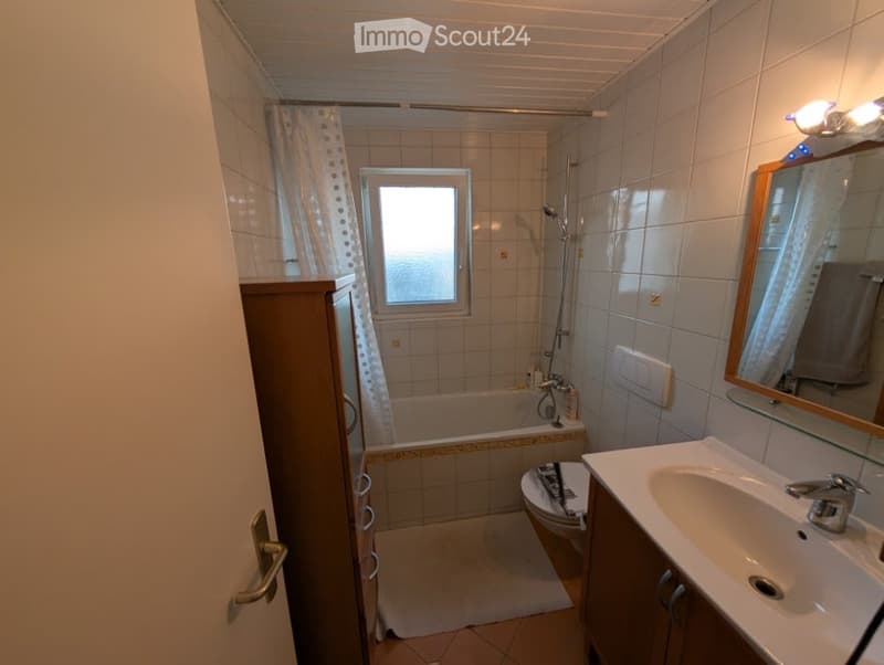 Bathroom with a bathtub, toilet, sink, mirror, shower, and cabinet. The room features tiled walls and a window with a curtain.