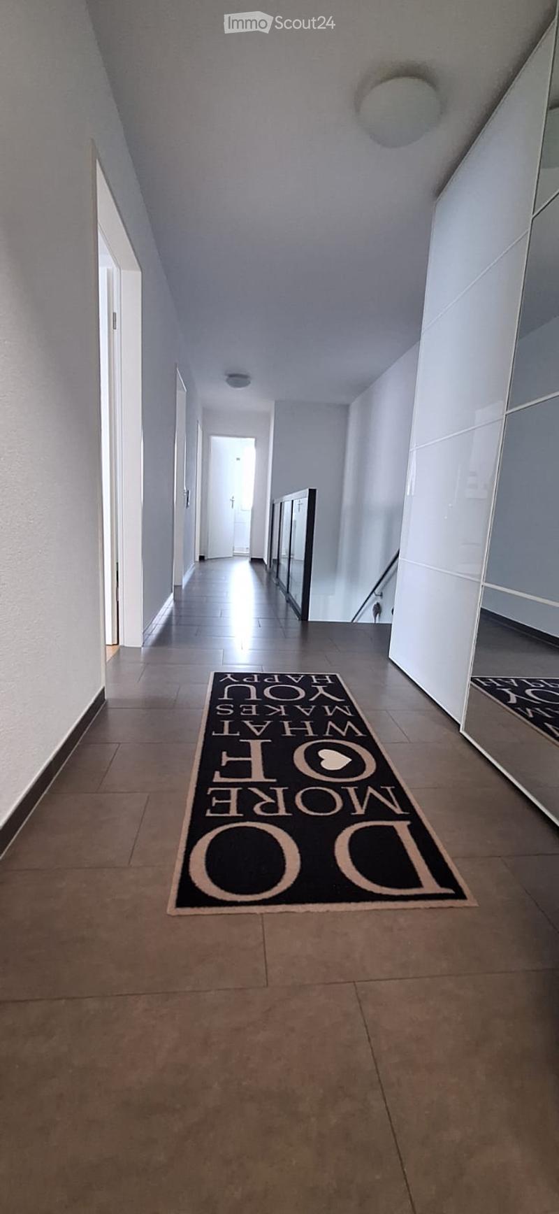A clean, modern hallway with tiled flooring, white walls, and a decorative welcome mat reading "HOME" in the center.