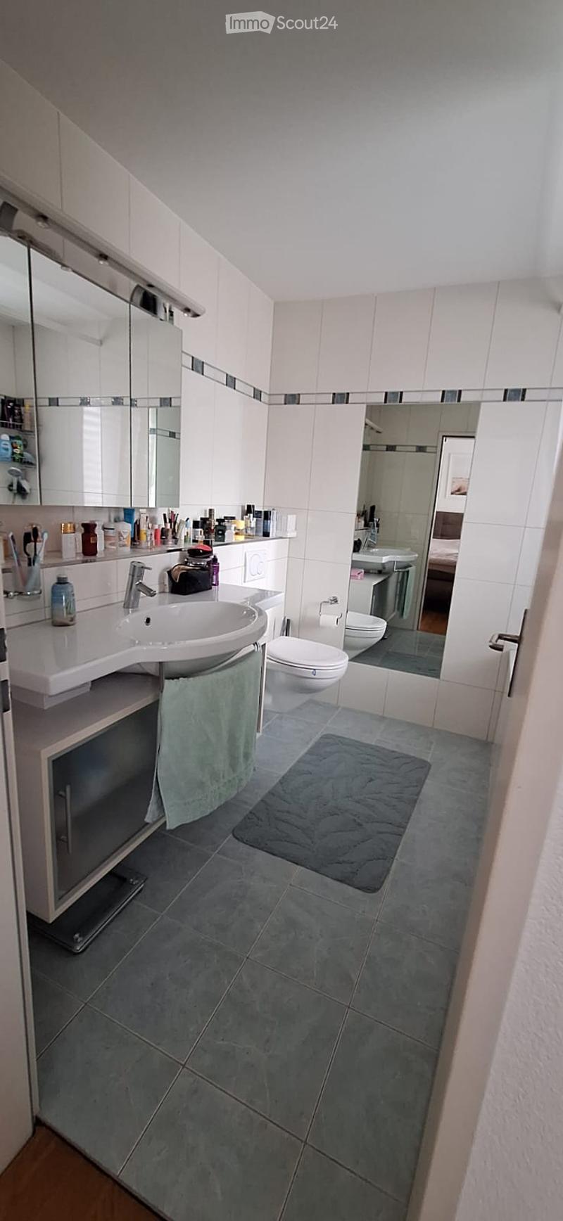 Modern bathroom with white tiles, a sink, toilet, mirror, and a towel on the floor.