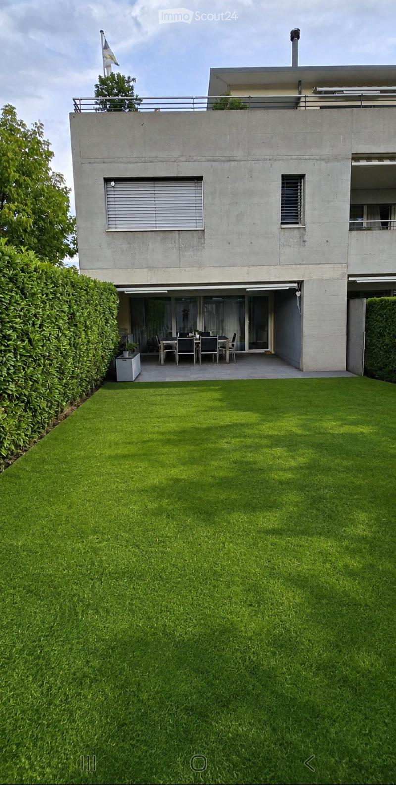 Modern house with a well-maintained lawn, a small patio area with a dining set, and a flagpole on the roof.
