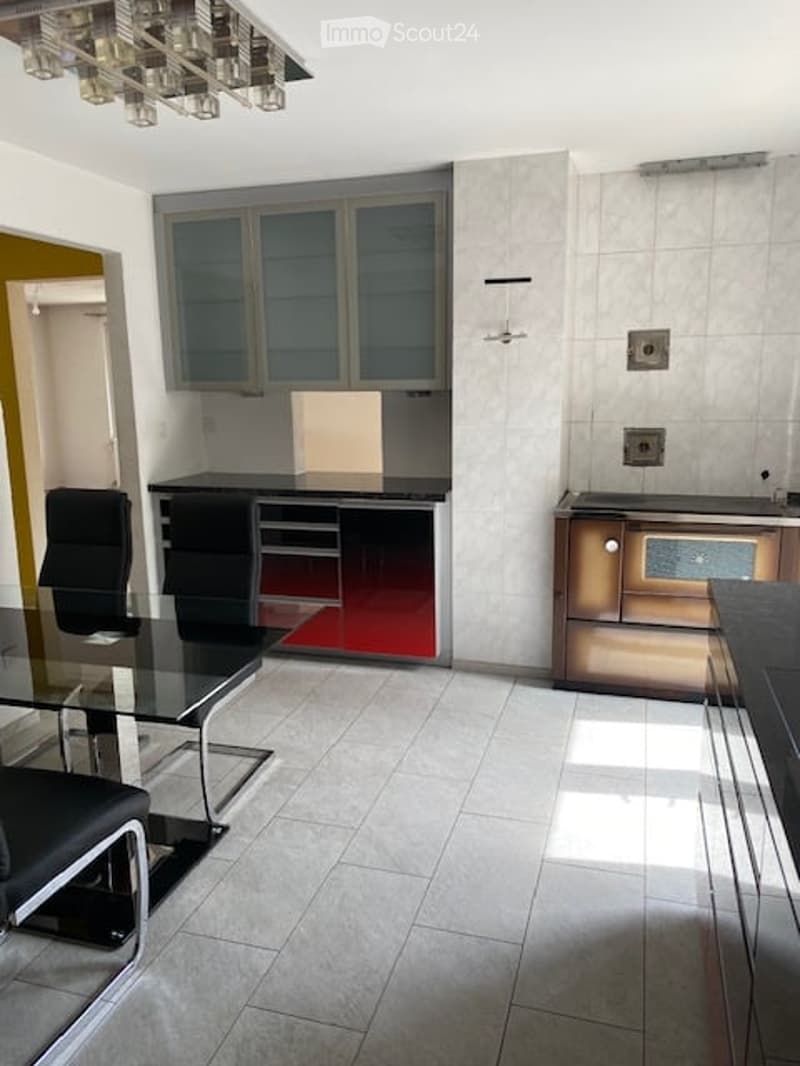 Modern kitchen with grey cabinets, black countertops, a glass dining table with black chairs, and a built-in oven.