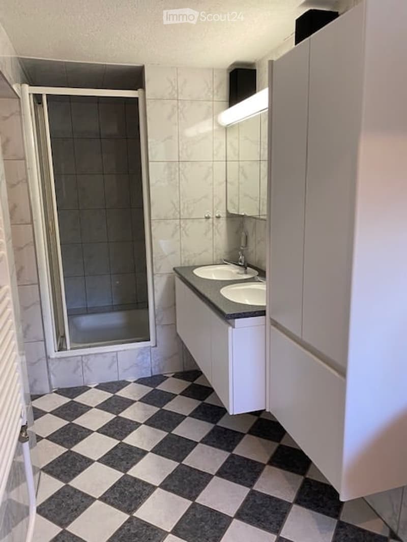 Modern bathroom with a black and white checkered floor, white tiled walls, a double sink vanity with mirrored cabinet, and a glass-enclosed shower stall.
