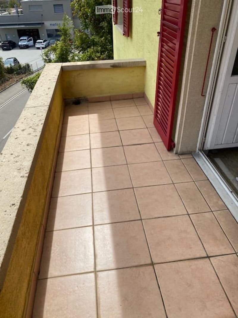 Balcony with tiled floor, wooden railing, and red shutters on the adjacent wall.