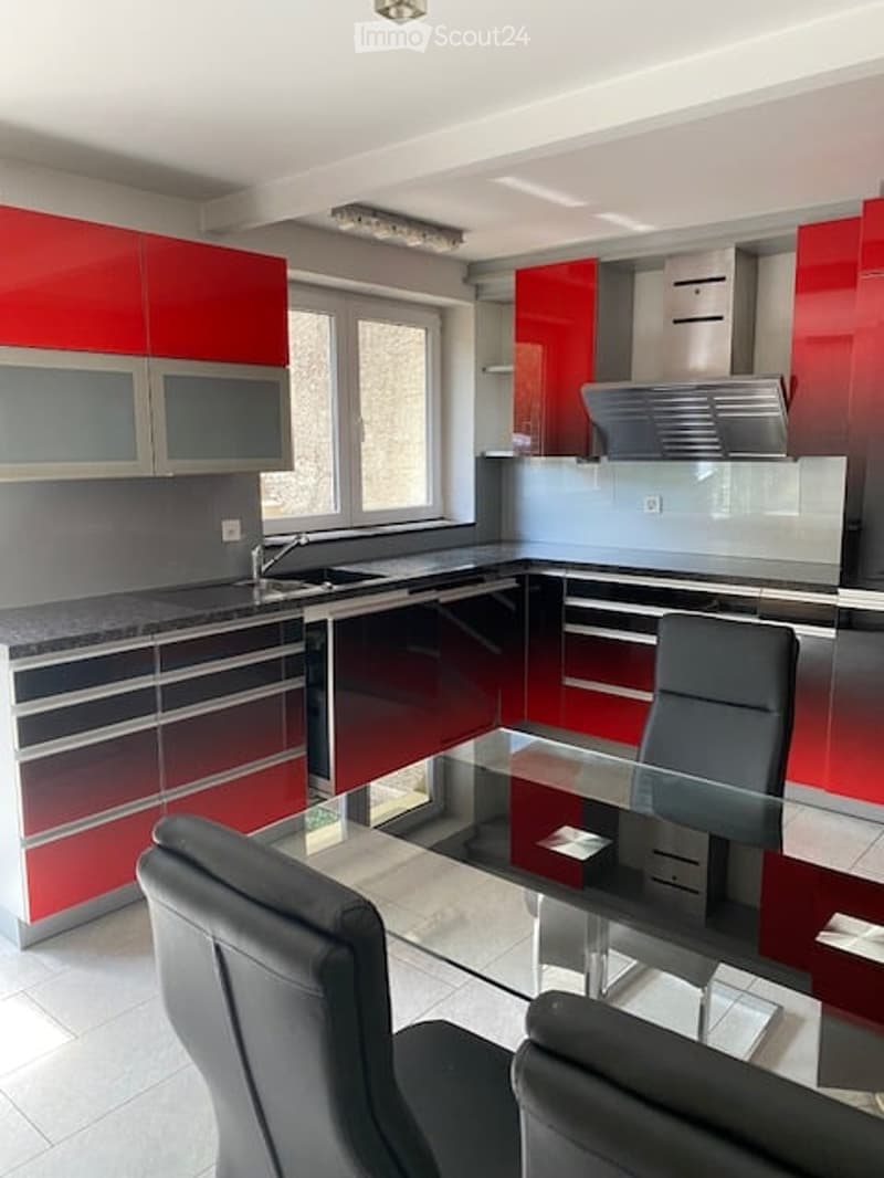 Modern kitchen with red and grey cabinets, a central island, and a glass dining table with two chairs.