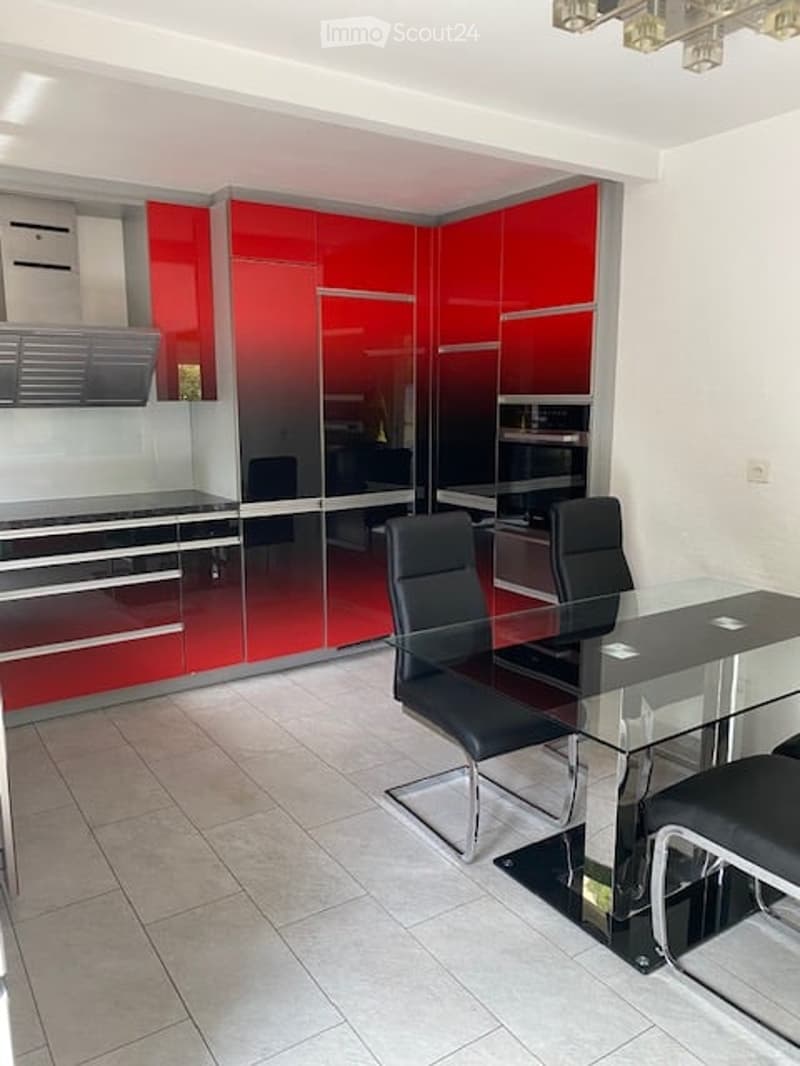 Modern kitchen with red and black cabinets, a glass dining table, and black chairs.