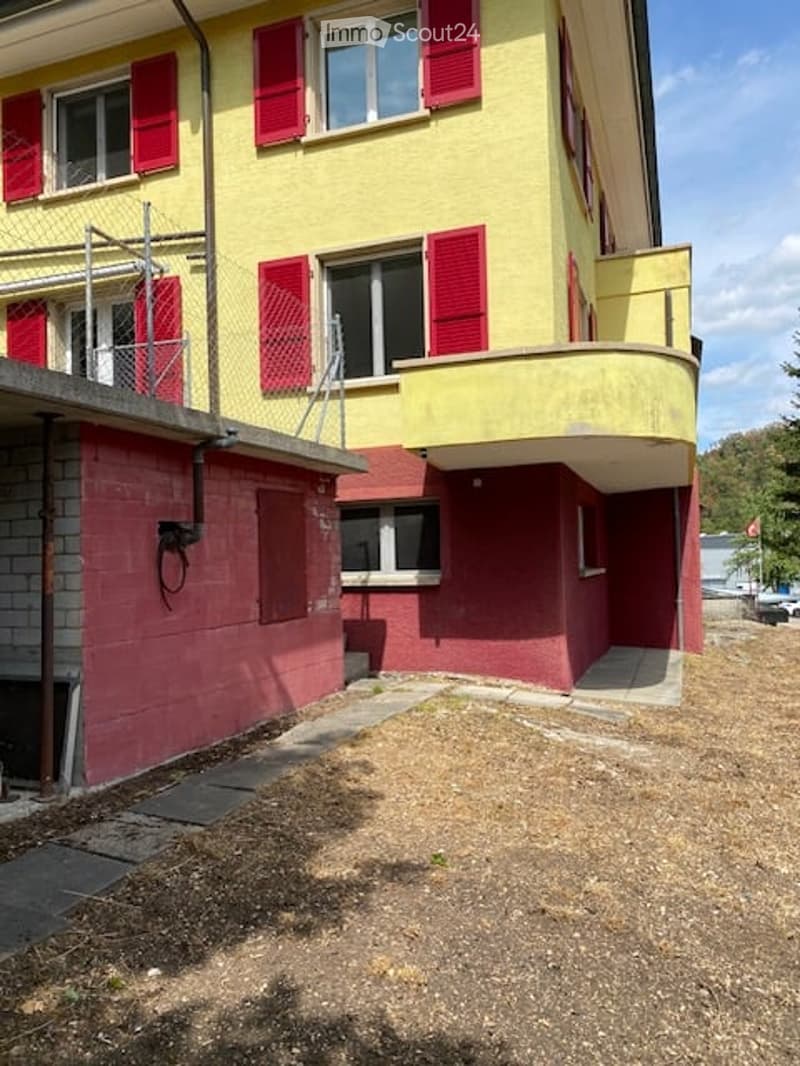 Two-story building with yellow and red exterior, multiple windows with shutters, and a balcony on the upper level.