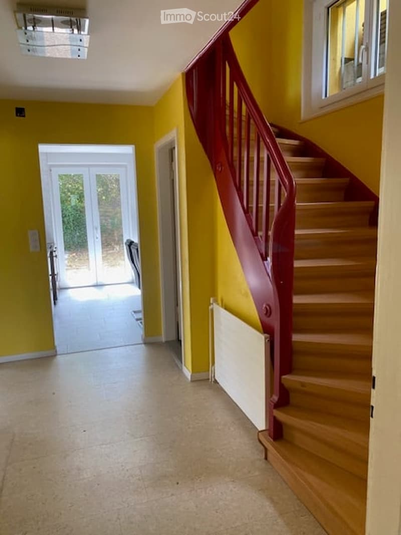 Bright hallway with yellow walls, wooden staircase with red railing, and a glass door leading to an outdoor area.