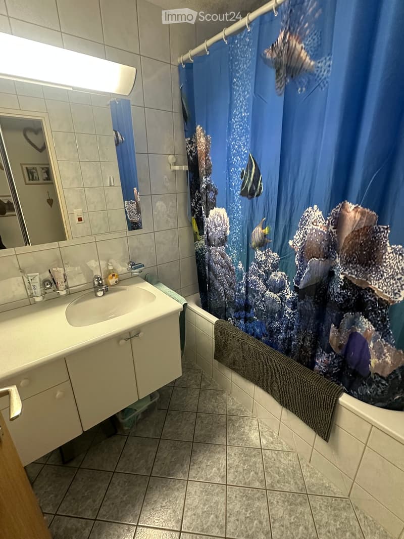 Bathroom with a white sink, mirror, and a bathtub with a blue ocean-themed shower curtain. A towel is draped over the edge of the tub.