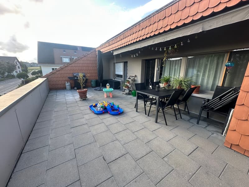 Balcony with tiled floor, outdoor furniture including a table and chairs, potted plants, and children's toys.