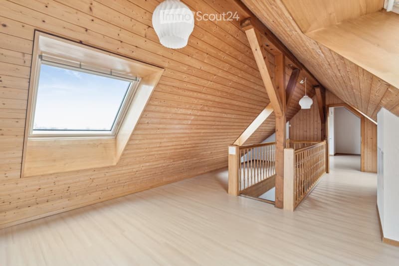 Bright, wooden-floored hallway with slanted wooden ceiling, large skylight window, and staircase leading upwards.