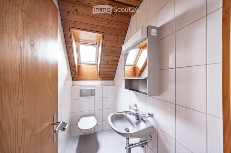 Modern bathroom with white tiles, wooden ceiling, skylight window, toilet, sink, mirror, and cabinet.