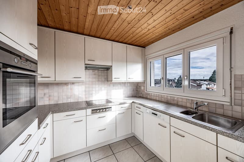 Modern kitchen with white cabinets, granite countertops, stainless steel oven, and sink. Large windows provide natural light and a view of the surroundings.