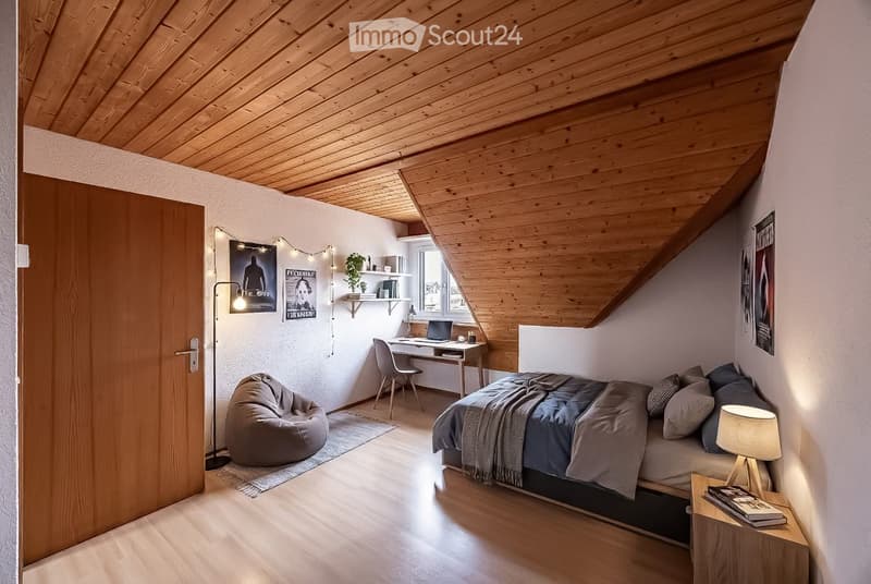 Cozy attic bedroom with wooden slanted ceilings, a bed, desk, beanie chair, and shelves with books and decor.