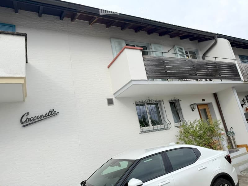 Two-story white building with balcony, windows, and a parked car in front.