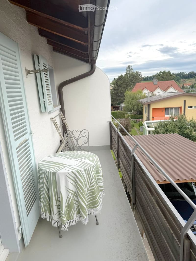 Balcony with a table and chair, wooden railing, and a view of the surrounding area.