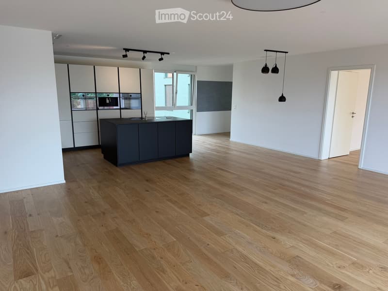 Empty room with light wooden flooring, white walls, and modern cabinetry in the background. No furniture or appliances are present.