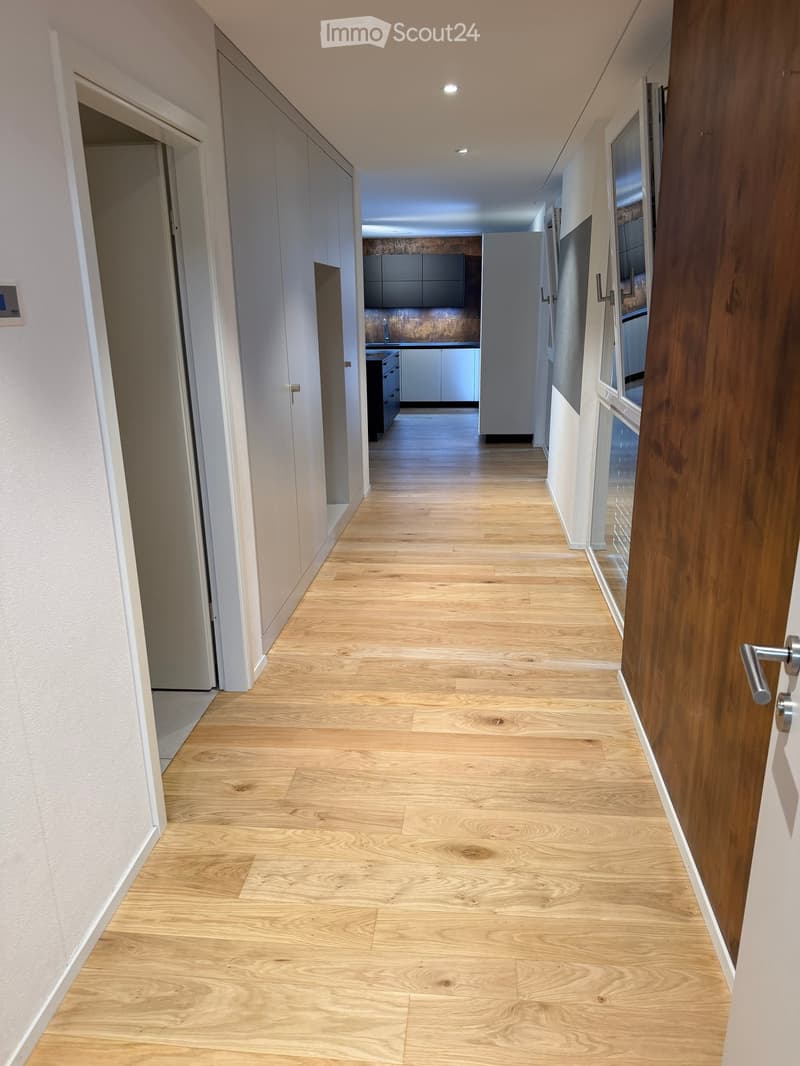 Empty hallway with light wooden flooring, white walls, and several doors leading to other rooms.