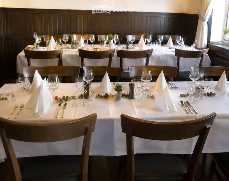 Restaurant dining area with multiple tables set for guests, each with white tablecloths, wine glasses, napkins, cutlery, candles, and small decorative plants.