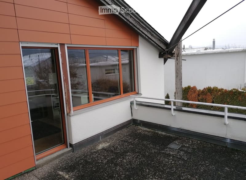 Balcony with a metal railing, glass door leading to the interior, and a view of neighboring buildings and trees.