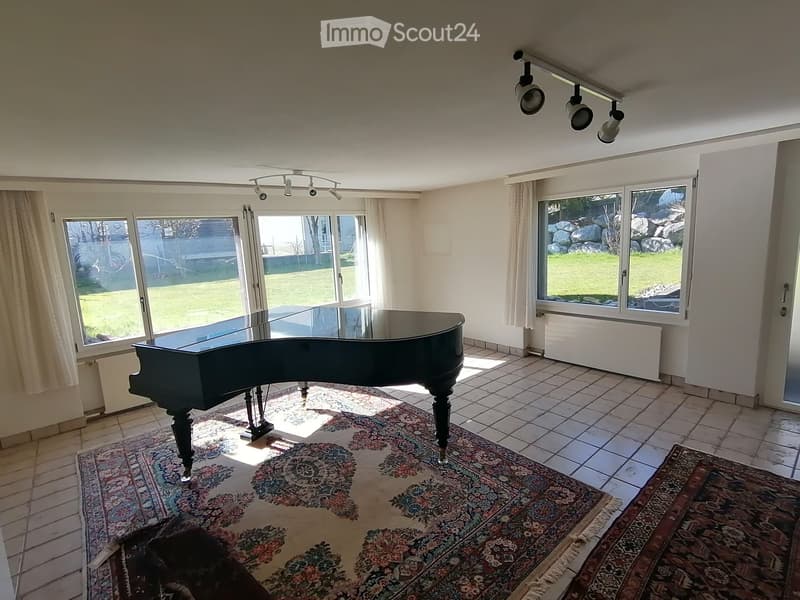 Bright room with large windows, tiled floor, and a grand piano on a patterned rug.