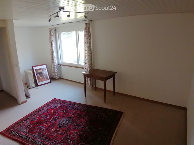 A room with a wooden table, a large picture frame, a fan, and a patterned rug on the floor.
