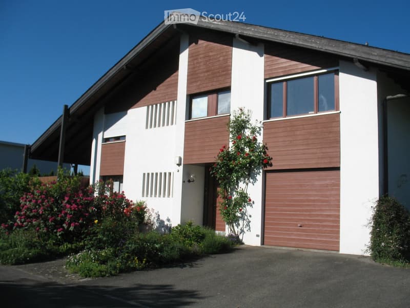 Modern two-story house with white and brown exterior, garage, and well-maintained garden with flowering plants.