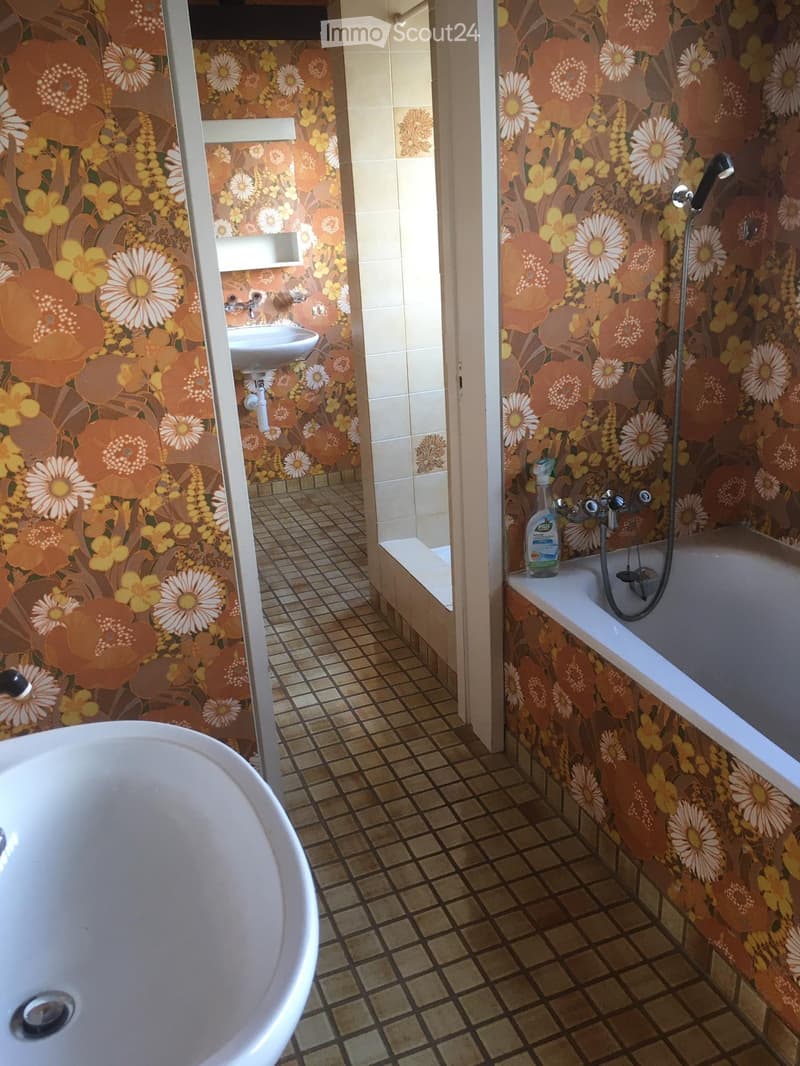 Bathroom with floral wallpaper, tiled floor, bathtub, sink, and showerhead.