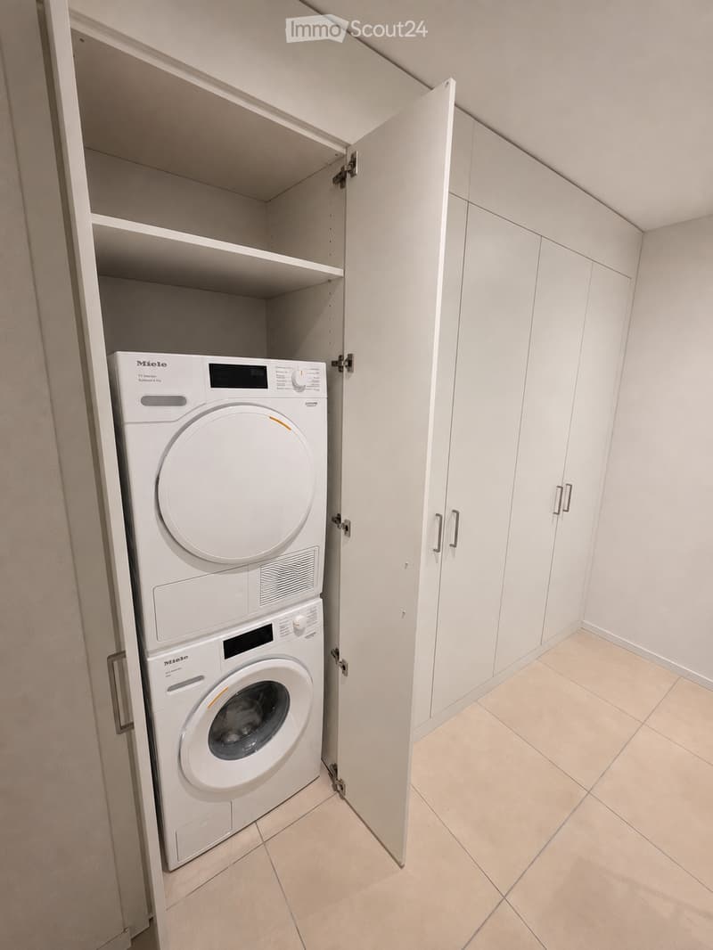 A compact bathroom with a built-in laundry area featuring a white washing machine and dryer unit within a cabinet.