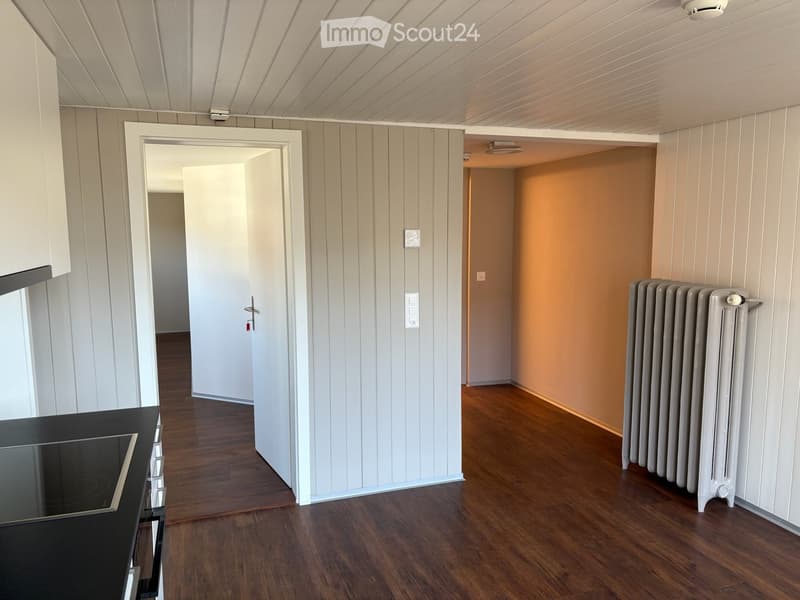 An empty room with wooden floors, white walls, and a door leading to another room. There is a radiator on the right side of the room.