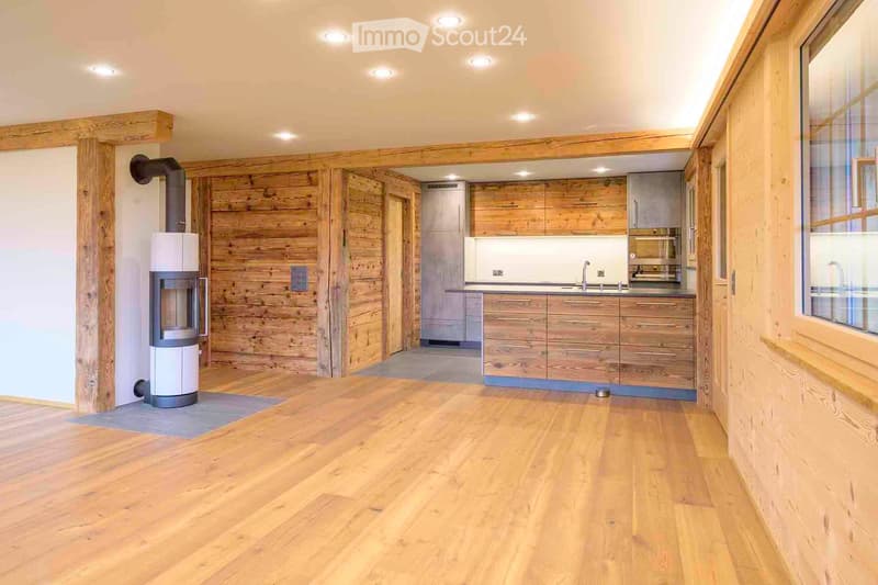 A modern kitchen with wooden cabinets, a sink, a faucet, a refrigerator, and a fireplace, featuring a wooden floor and wooden wall.