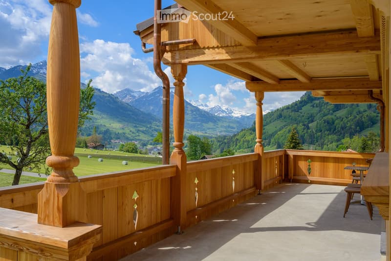 Wooden balcony with a scenic mountain view, featuring a table and chairs.