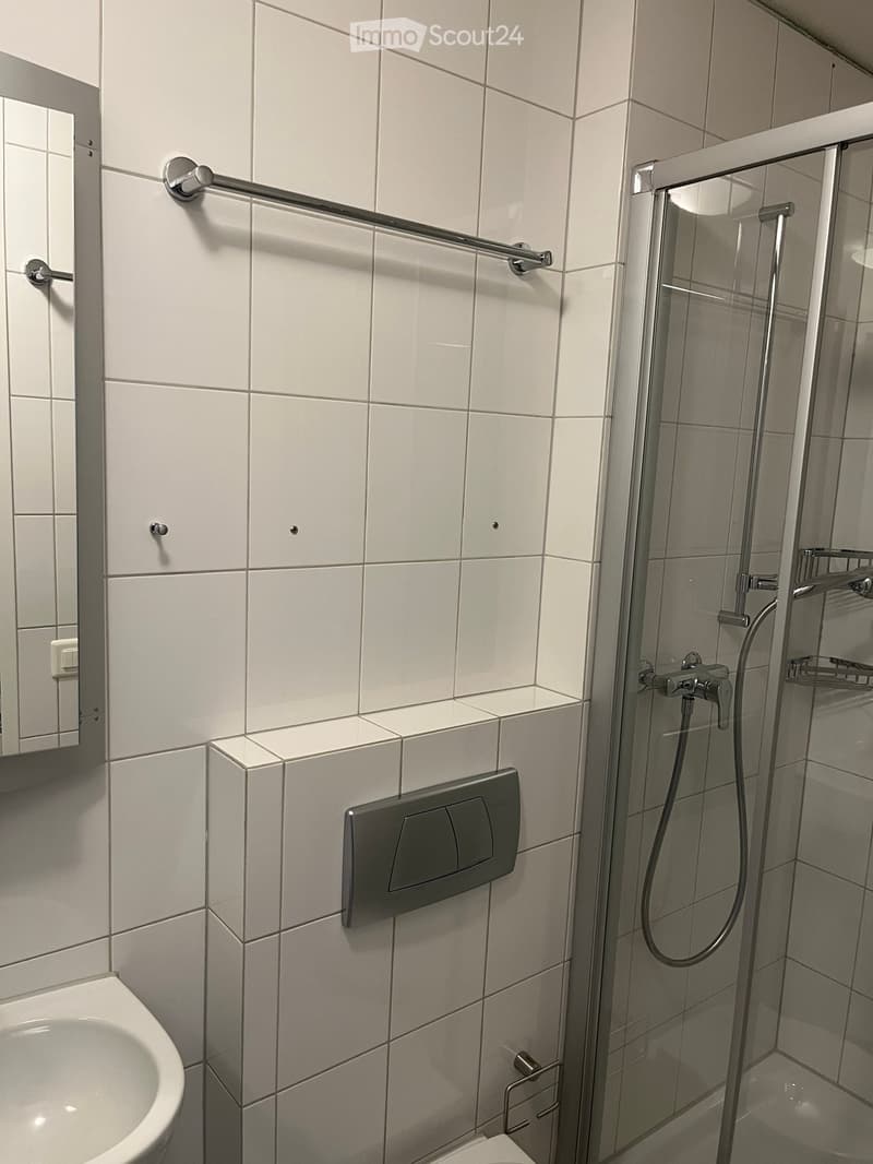 Modern bathroom with white tiled walls, a toilet, a sink, a glass-enclosed shower, and a towel rack.