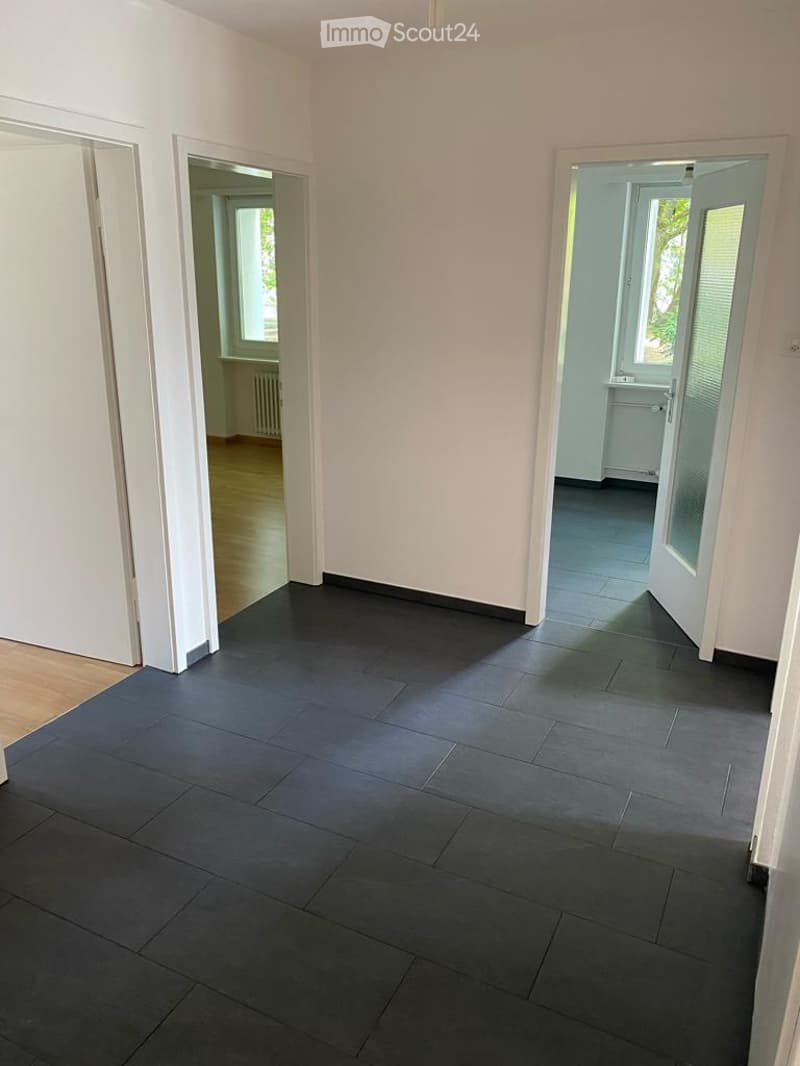 Empty room with dark grey tiled floor, white walls, and multiple doorways leading to other rooms.