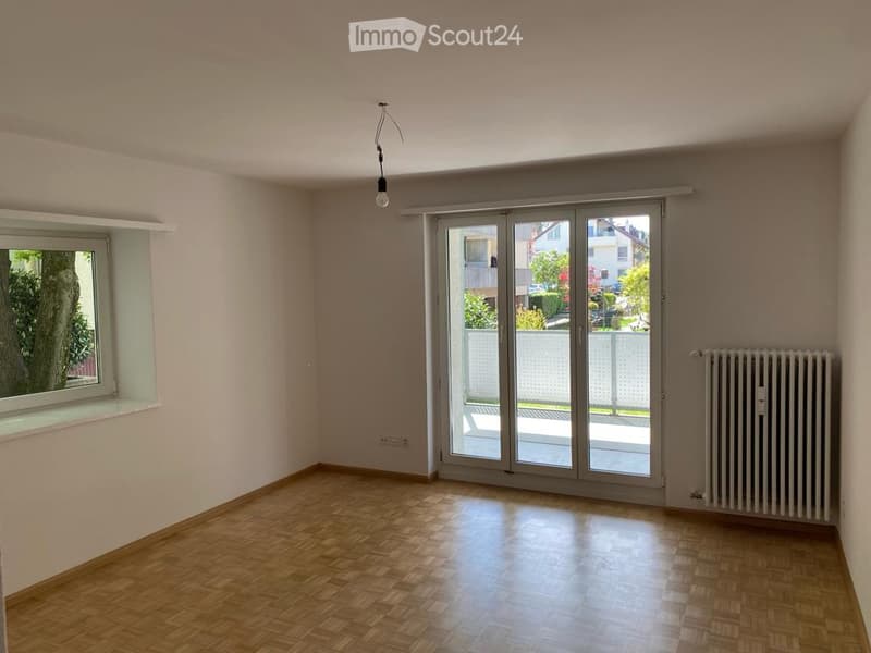 Empty room with wooden flooring, large sliding glass doors leading to a balcony, and a radiator on the wall.