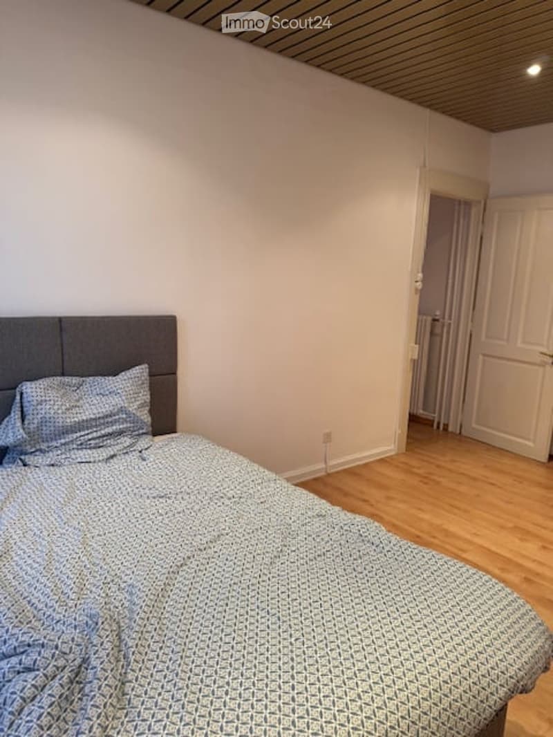 A bed with blue bedding, wooden floor, white walls, gray headboard, white door