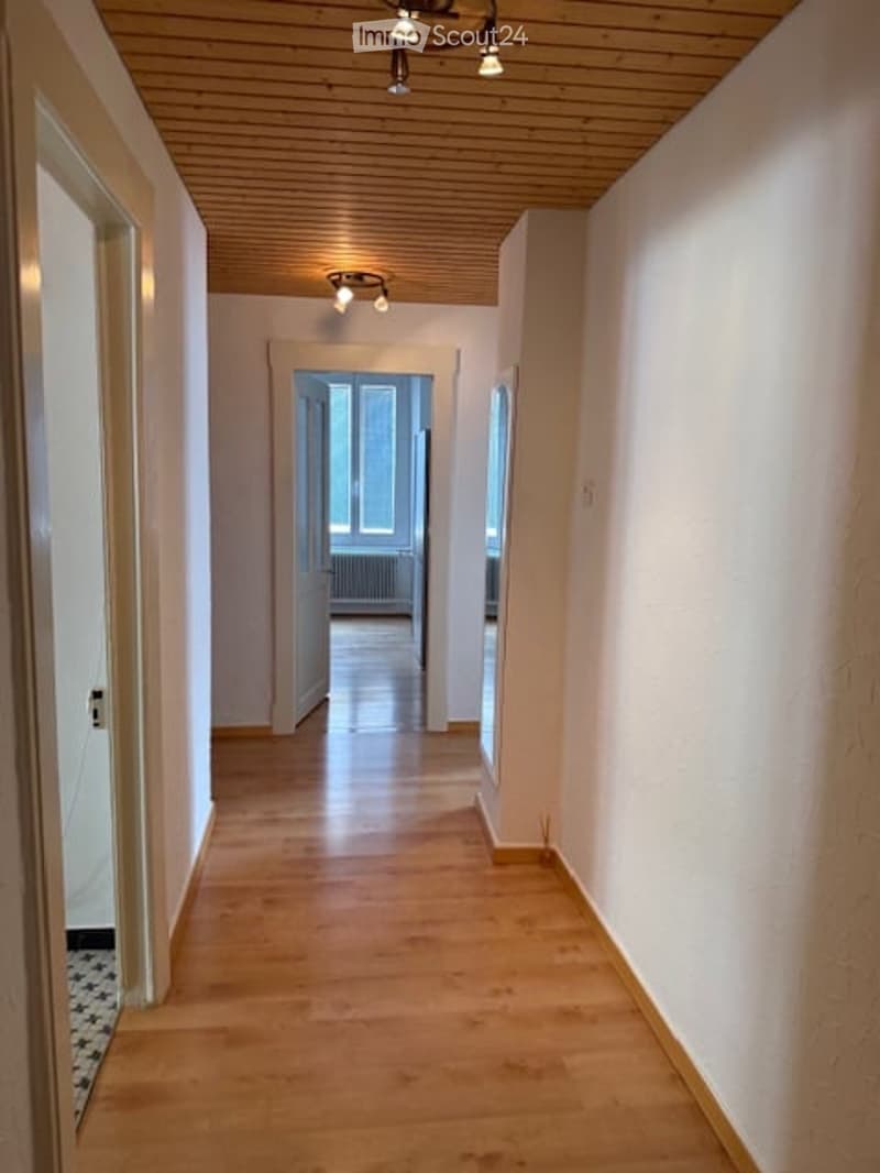 empty hallway with wooden floor and white walls, light fixtures on the ceiling, two doors on both sides, small windows
