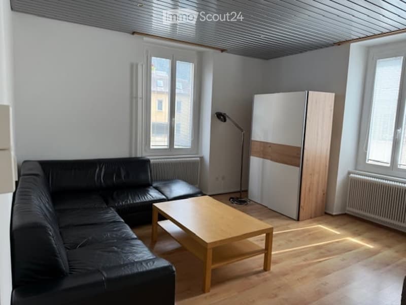 black sofa, wooden coffee table, wooden cabinet, floor lamp, white radiator, windows with white blinds