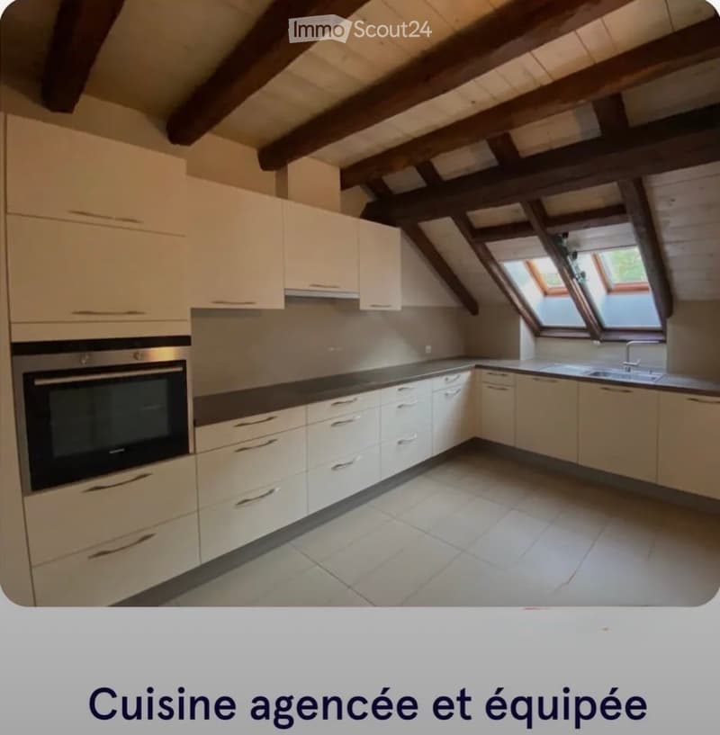 Modern kitchen with white cabinets, stainless steel oven, and a sink with a faucet. The ceiling features exposed wooden beams and skylights.