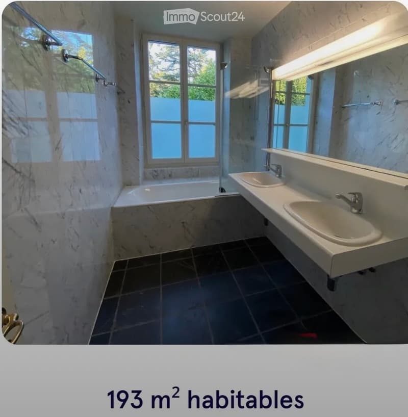Modern bathroom with marble walls and floors, a bathtub, double sink, and large windows.