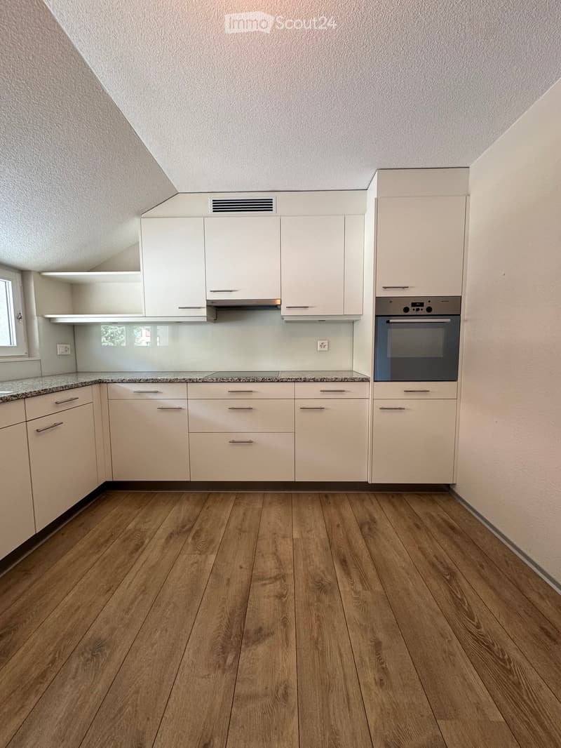Modern kitchen with white cabinets, granite countertop, and wooden flooring. Features an oven and built-in ventilation hood.